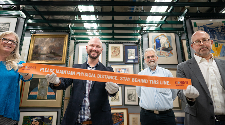 Jacqueline deVries, Stewart Van Cleve, Mike Bloomberg, and Michael Lansing hold a COVID-19 distancing floor sticker used at Augsburg, now filed in the university archives.